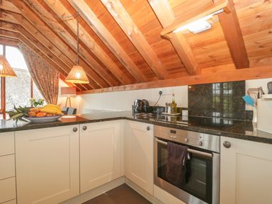 A kitchen with wooden ceiling beams white cabinets and stainless steel oven with fruit bowl on counter at Floras Barn in Crowcombe