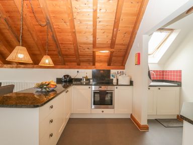 A kitchen with white cabinets black countertops wooden ceiling and two hanging lamps at Floras Barn in Crowcombe