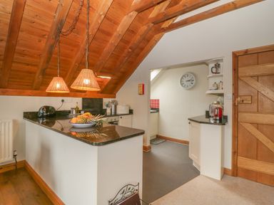 A kitchen with a wooden ceiling two pendant lights a fruit bowl on the counter and a wooden door at Floras Barn in Crowcombe
