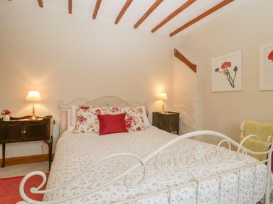 A bedroom with a white metal bed frame floral bedding two bedside tables with lamps and flower paintings on the wall at Floras Barn in Crowcombe