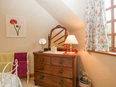 A bedroom corner with a wooden dresser a mirror table lamp floral curtains and a towel rack at Floras Barn in Crowcombe