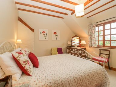 A bedroom with a bed a dresser with mirror two chairs floral curtains and wall art at Floras Barn in Crowcombe