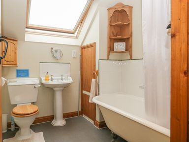 A bathroom with a toilet a pedestal sink a bathtub with shower curtain and wooden shelves at Floras Barn in Crowcombe