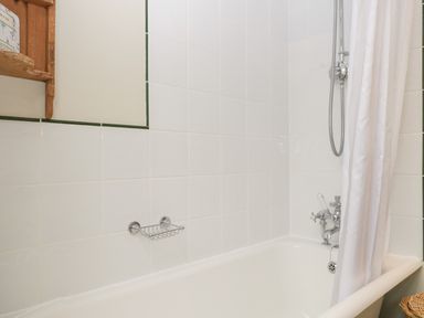 A bathroom with a white bathtub white tiled walls a showerhead a shower curtain and a small wall-mounted soap holder at Floras Barn in Crowcombe