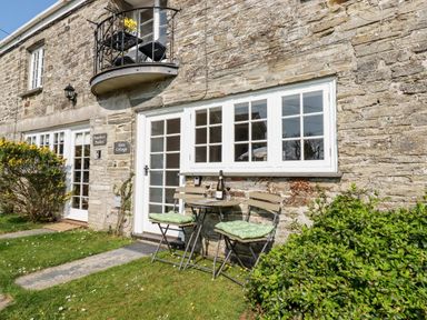 A stone cottage exterior with white framed windows and a small patio table with two chairs on grass at Slate Cottage Tredethy near Bodmin Moor