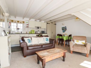 A living room with a brown leather sofa, wooden coffee table, armchair, dining table with green tablecloth and kitchen area at Slate Cottage in Tredethy near Bodmin Moor