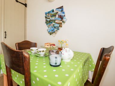 A dining table with a green polka dot tablecloth set with tea cups milk jug and cake with wooden chairs at Slate Cottage in Tredethy near Bodmin Moor