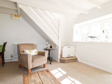 A sitting area with a striped armchair a small round table a wooden coffee table and stairs next to a window at Slate Cottage in Tredethy near Bodmin Moor