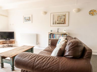 A living room with a brown leather sofa wooden coffee table TV and bookshelf at Slate Cottage Tredethy near Bodmin Moor