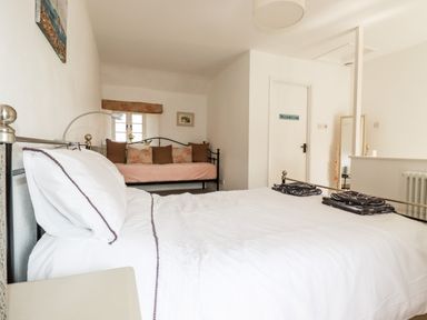 A bedroom with a double bed white linens a daybed with cushions a door labeled washroom and a floor mirror at Slate Cottage in Tredethy near Bodmin Moor