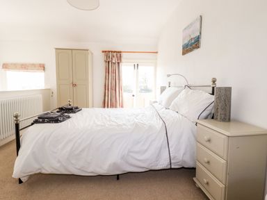 A bedroom with a double bed bedside table wardrobe and floral curtains at Slate Cottage in Tredethy near Bodmin Moor