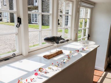 A window sill with a whale sculpture colorful beads and a glass bowl at Slate Cottage in Tredethy near Bodmin Moor