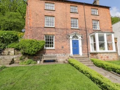 The front exterior of a brick house with a blue door a stone pathway and green bushes at Viaduct House in Lydbrook