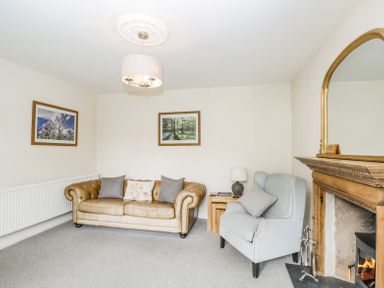 A living room with a leather sofa and armchair beside a wooden fireplace and framed pictures on the wall at Viaduct House in Lydbrook