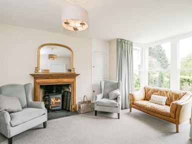A living room with two armchairs a leather sofa a fireplace with a mirror above and large windows with curtains at Viaduct House in Lydbrook
