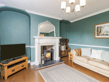 A living room with a leather sofa a wood burning stove in a fireplace a TV on a wooden stand and a rug on a wooden floor at Viaduct House in Lydbrook