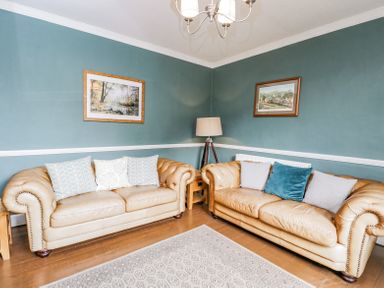 A living room with two beige leather sofas cushions a floor lamp wooden side tables and framed pictures on a teal wall at Viaduct House in Lydbrook