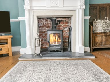 A fireplace with a burning stove surrounded by a white mantle in a room with wooden floor and rug at Viaduct House in Lydbrook