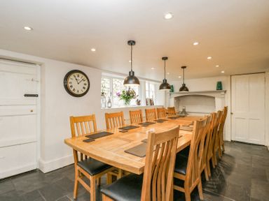 A dining room with a long wooden table and wooden chairs under pendant lights at Viaduct House in Lydbrook