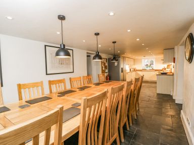 A dining area with a long wooden table and chairs next to a kitchen with cabinets and appliances at Viaduct House in Lydbrook