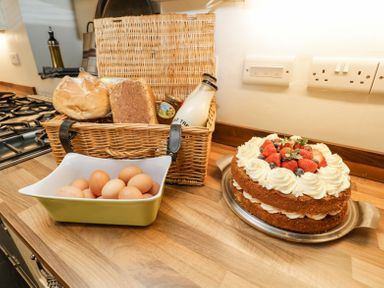 A kitchen counter with a basket containing bread milk and jam a dish of eggs and a cake with cream and strawberries on a tray at Viaduct House in Lydbrook