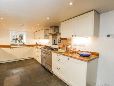 A kitchen with white cabinets wooden countertops a stove window with flowers and cakes on the counter at Viaduct House in Lydbrook