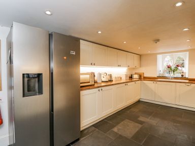 A kitchen with white cabinets wooden countertops a stainless steel refrigerator and a window with flowers at Viaduct House in Lydbrook