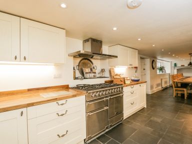 A kitchen with white cabinets wooden countertops a stainless steel stove and dining table at Viaduct House in Lydbrook