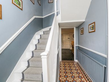 A hallway with blue walls a patterned tile floor a staircase with grey carpet and metal stair rods at Viaduct House in Lydbrook