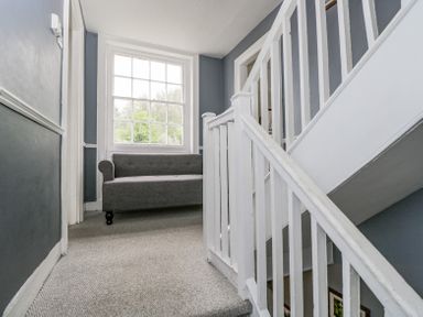A staircase landing with a gray sofa near a large window at Viaduct House in Lydbrook