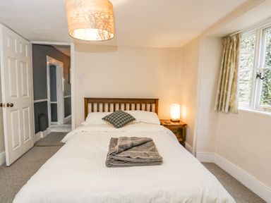 A bedroom with a double bed a nightstand with a lamp a window with curtains and an open door at Viaduct House in Lydbrook