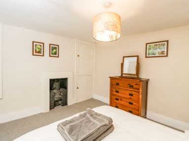 A bedroom with a wooden dresser with mirror folded towels on bed and framed pictures on walls at Viaduct House in Lydbrook