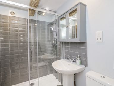 A bathroom with a glass shower enclosure gray tiled walls a white pedestal sink a mirrored cabinet and a white toilet at Viaduct House in Lydbrook