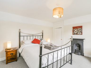 A bedroom with a metal bed frame white bedding a wooden nightstand with a lamp folded towels on the bed a fireplace and a painting at Viaduct House in Lydbrook