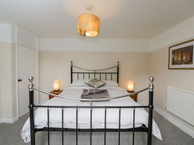 A bedroom with a metal bed frame bedside tables with lamps a folded towel and a framed picture on the wall at Viaduct House in Lydbrook