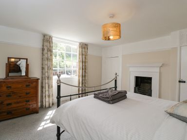 A bedroom with a metal bed frame a wooden dresser with a mirror a window with curtains and a fireplace at Viaduct House in Lydbrook