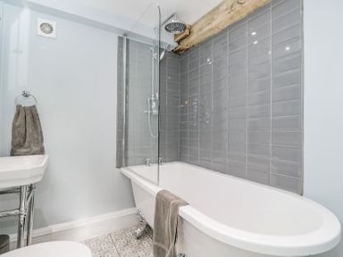 A bathroom with a freestanding bathtub a showerhead grey wall tiles and a towel hanging at Viaduct House in Lydbrook