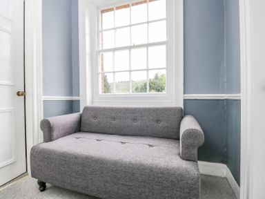 A gray fabric loveseat in front of a window with blue and white walls at Viaduct House in Lydbrook