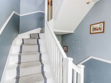 A staircase with white steps and grey carpet runner on blue walls with two framed pictures at Viaduct House in Lydbrook