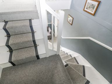 A staircase with gray carpet runners and white walls with framed pictures at Viaduct House in Lydbrook