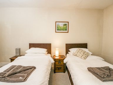 A bedroom with two single beds separated by a wooden nightstand and a lamp at Viaduct House in Lydbrook