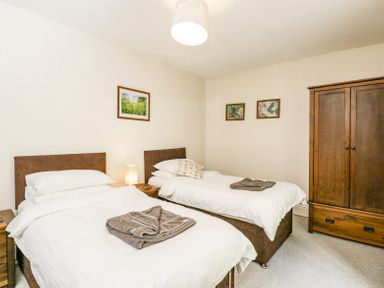 A bedroom with two single beds bedside tables a wooden wardrobe and framed pictures on walls at Viaduct House in Lydbrook
