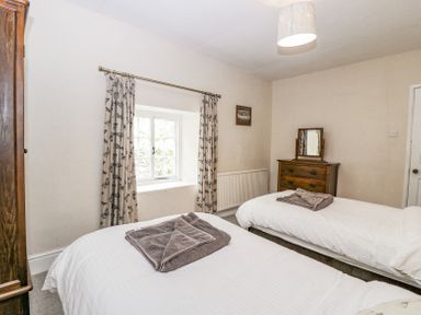 A bedroom with two single beds white bedding wooden dresser with mirror and window with patterned curtains at Viaduct House in Lydbrook