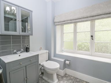 A bathroom with a toilet sink cabinet mirror window with blinds and patterned floor tiles at Viaduct House in Lydbrook