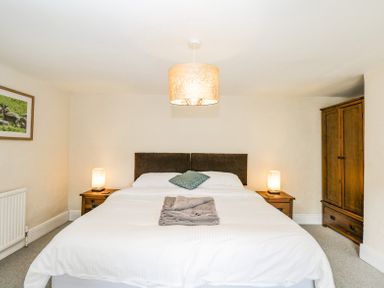 A bedroom with a double bed two bedside tables with lamps a wooden wardrobe and a framed picture on the wall at Viaduct House in Lydbrook
