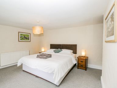 A bedroom with a double bed two bedside tables with lamps and framed pictures on the walls at Viaduct House in Lydbrook