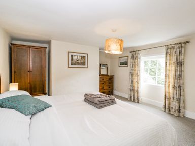 A bedroom with a bed towels on it a wooden wardrobe and chest of drawers with mirror and window with curtains at Viaduct House in Lydbrook