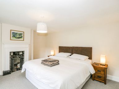 A bedroom with a large bed bedside tables lamps a fireplace and a framed picture at Viaduct House in Lydbrook