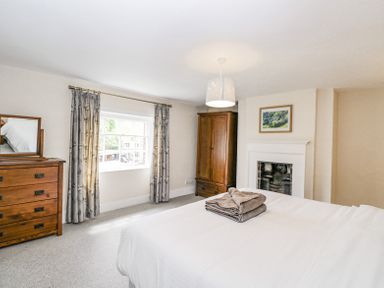 A bedroom with a bed folded towels wooden dresser with mirror wardrobe window with curtains and a fireplace at Viaduct House in Lydbrook