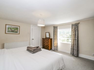 A bedroom with a bed covered in white linens towels on the bed a wooden dresser with a mirror a window with curtains and a framed picture on the wall at Viaduct House in Lydbrook